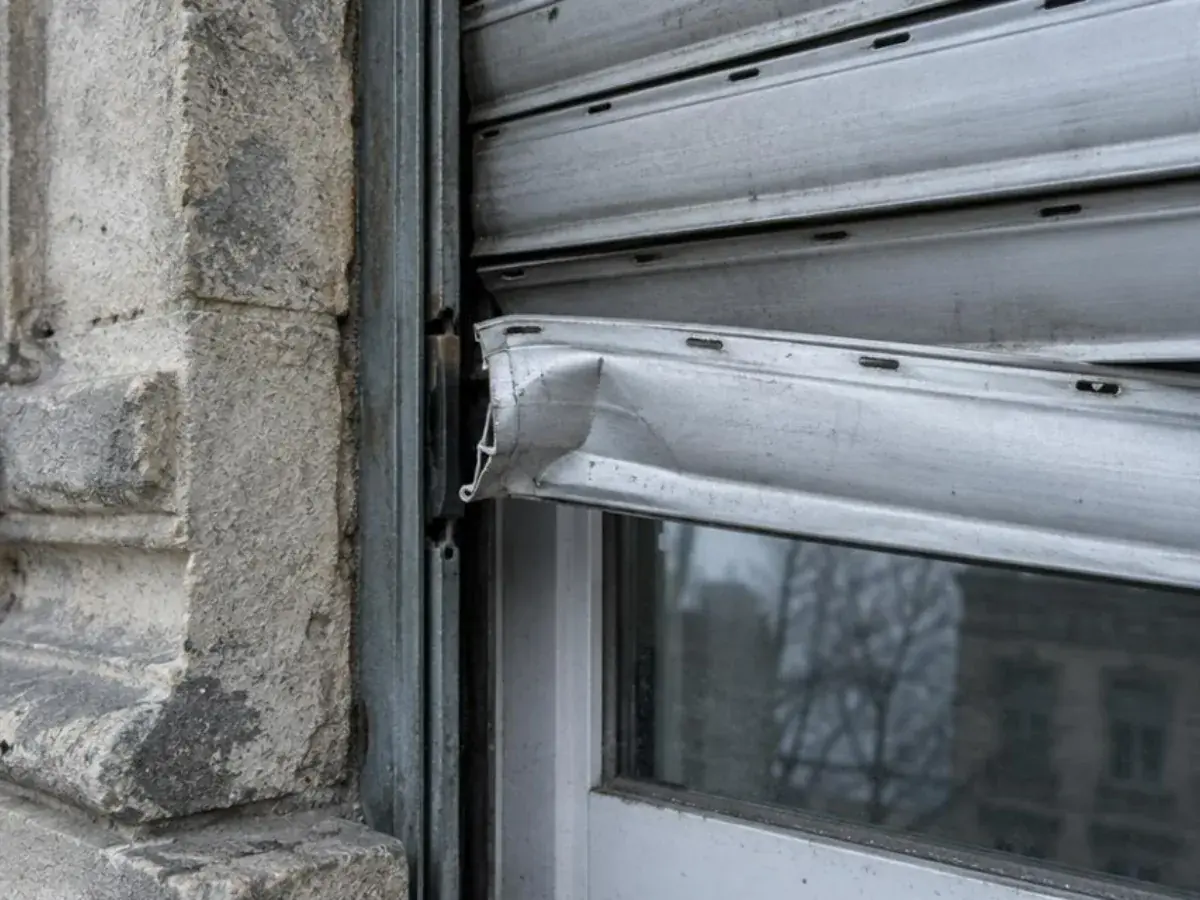 Lame de volet roulant en PVC blanc fendue sur toute sa longueur, vue de près devant une vitre
